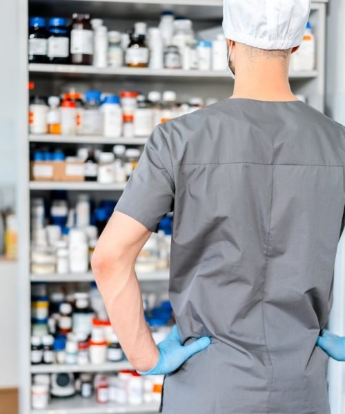 pexels-photo-9629685-9629685 Male pharmacist in surgical cap and gloves organizing shelves of medication in a pharmacy.